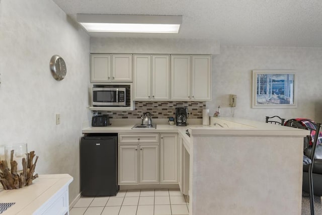 kitchen with black refrigerator, kitchen peninsula, decorative backsplash, sink, and light tile patterned floors