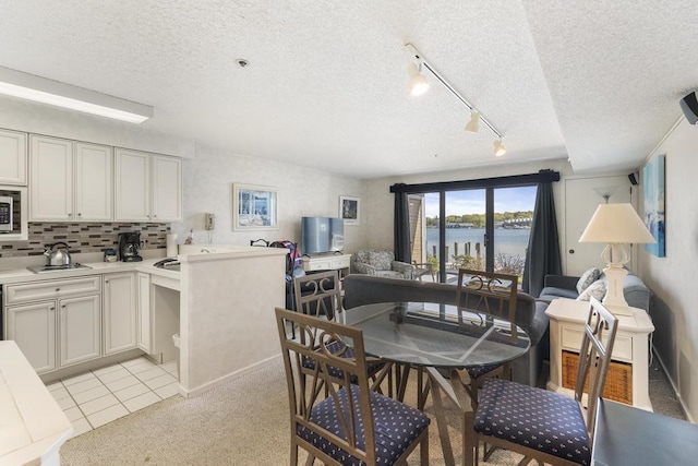 kitchen featuring tasteful backsplash, kitchen peninsula, track lighting, a textured ceiling, and light tile patterned flooring