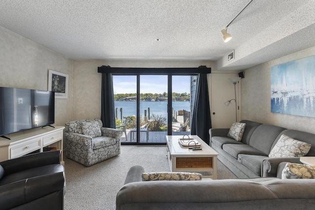 carpeted living room with rail lighting, a water view, and a textured ceiling