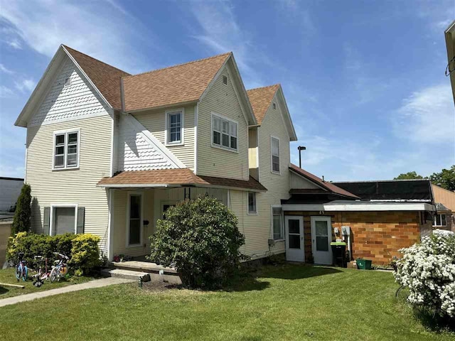 rear view of house featuring a lawn and roof with shingles