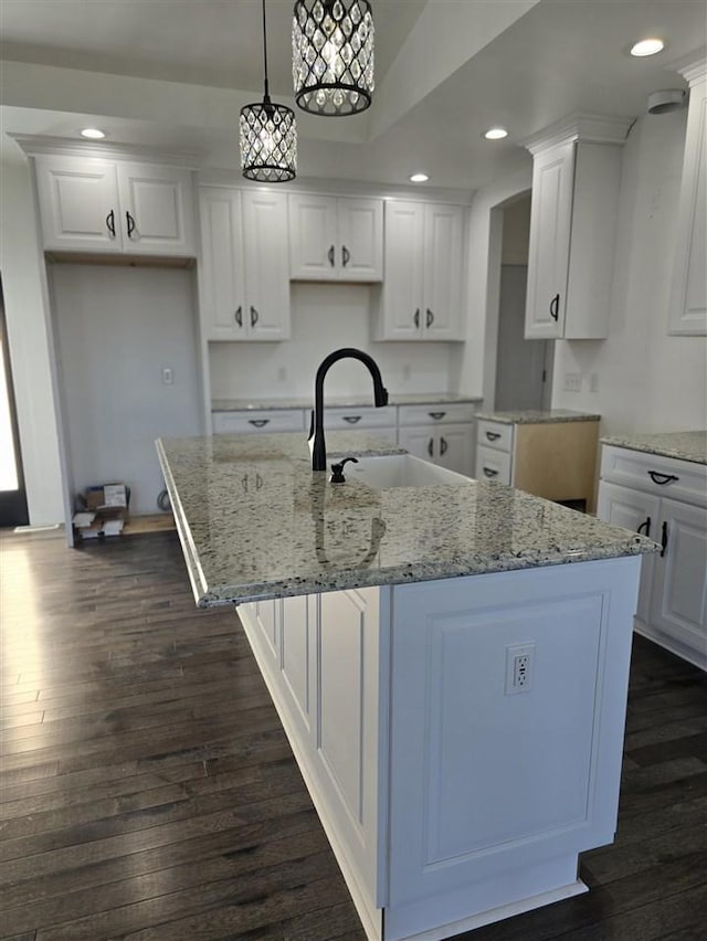 kitchen with a center island with sink, white cabinets, hanging light fixtures, and sink