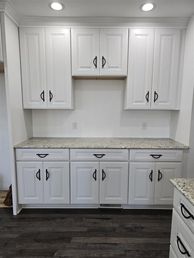 kitchen with light stone countertops, white cabinetry, and dark wood-type flooring