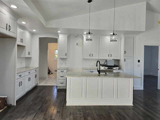 kitchen featuring light stone counters, vaulted ceiling, dark wood-type flooring, decorative light fixtures, and white cabinets