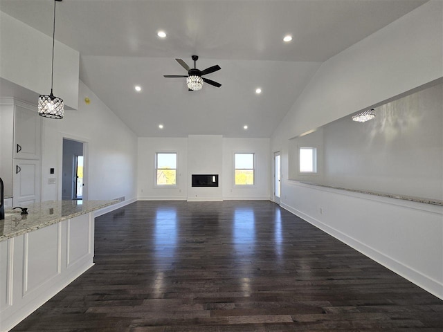 unfurnished living room with dark hardwood / wood-style floors, ceiling fan with notable chandelier, and high vaulted ceiling