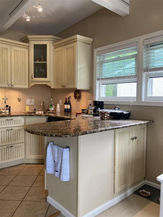 kitchen featuring sink, kitchen peninsula, dark stone countertops, cream cabinetry, and light tile patterned flooring