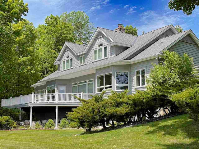 rear view of house featuring a deck, a yard, a chimney, and roof with shingles