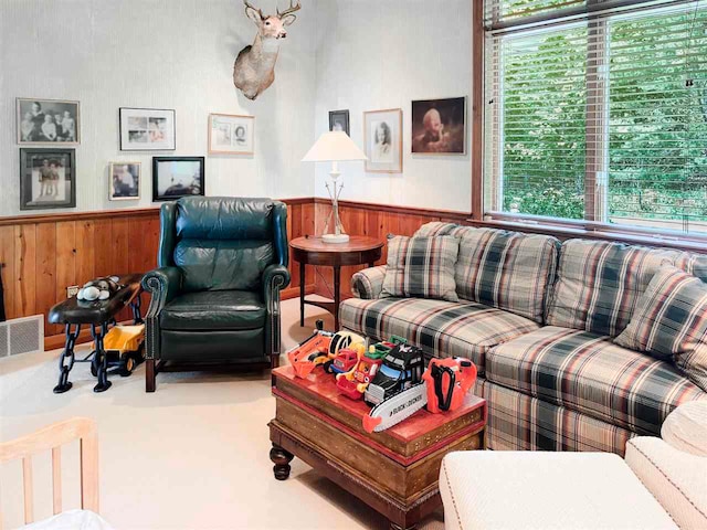 living area featuring wood walls, visible vents, carpet flooring, and wainscoting