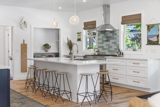 401 Antrim St, Charlevoix, MI 49720 - kitchen with wall chimney range hood, a sink, white cabinetry, a breakfast bar area, and light wood finished floors