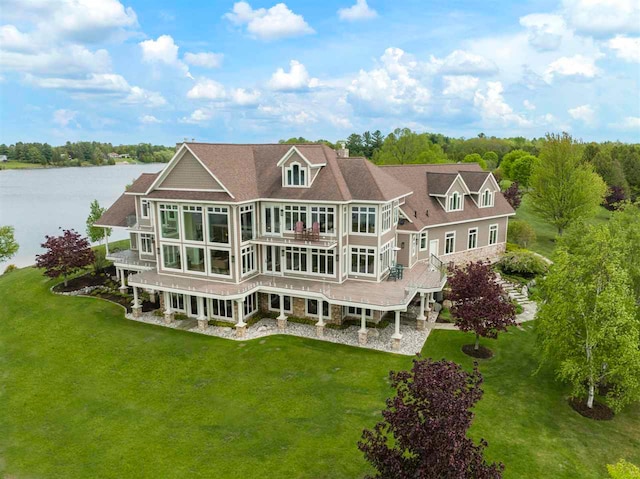 rear view of house with a deck with water view and a lawn