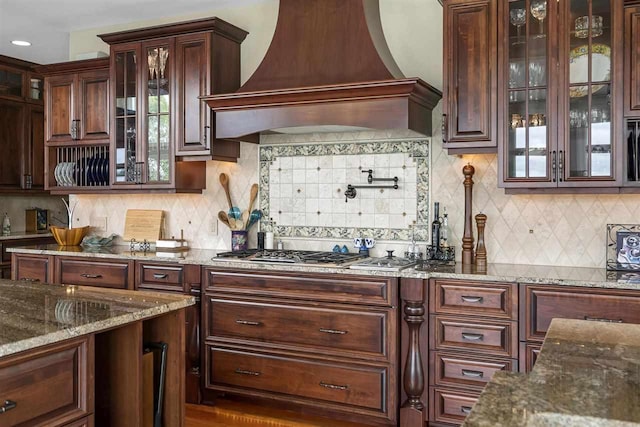 1439 Lindburgh Ln, Cheboygan, MI 49721 - kitchen with premium range hood, tasteful backsplash, stone countertops, glass insert cabinets, and recessed lighting