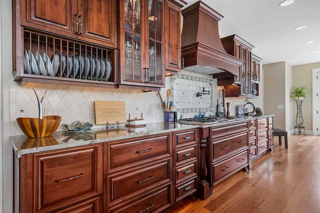 kitchen with light stone countertops, tasteful backsplash, wood-type flooring, premium range hood, and stainless steel gas cooktop