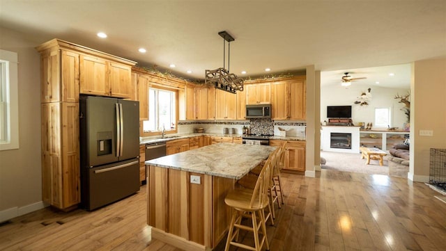 kitchen with ceiling fan with notable chandelier, a kitchen island, stainless steel appliances, decorative backsplash, and light hardwood / wood-style flooring