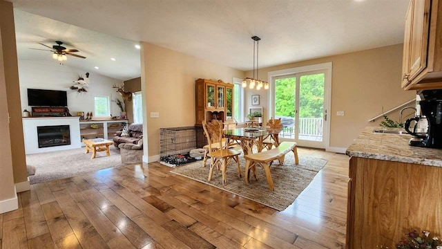 dining room featuring light wood-type flooring, vaulted ceiling, ceiling fan with notable chandelier, and sink