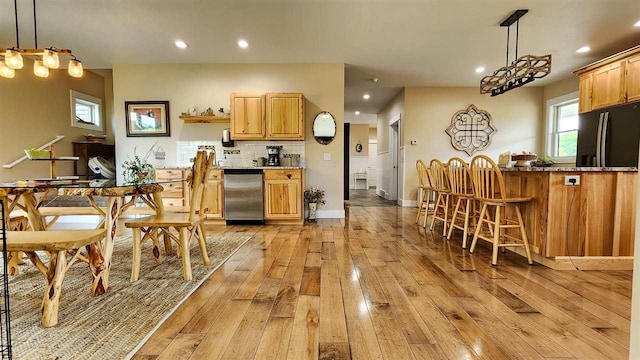 kitchen with backsplash, hanging light fixtures, dishwasher, and light hardwood / wood-style flooring