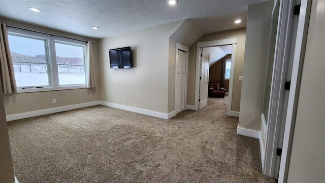 spare room featuring a textured ceiling, vaulted ceiling, and carpet floors