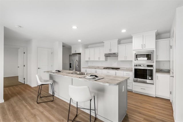 kitchen featuring light hardwood / wood-style floors, a center island with sink, white cabinets, sink, and appliances with stainless steel finishes