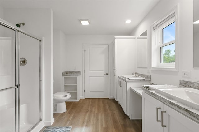 bathroom with hardwood / wood-style floors, double sink vanity, toilet, and a shower with door