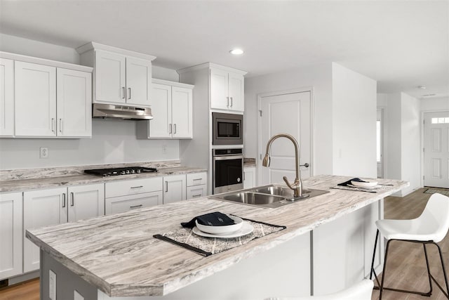 kitchen with appliances with stainless steel finishes, an island with sink, white cabinets, hardwood / wood-style floors, and sink