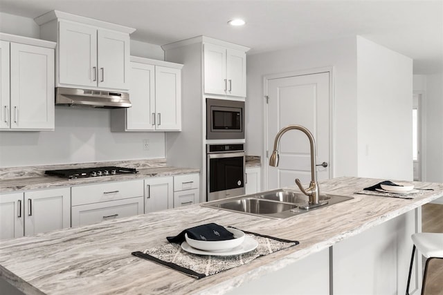 kitchen with light stone countertops, white cabinets, sink, a breakfast bar, and appliances with stainless steel finishes