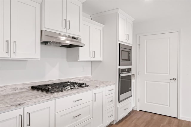 kitchen featuring appliances with stainless steel finishes, white cabinets, wood-type flooring, and light stone counters