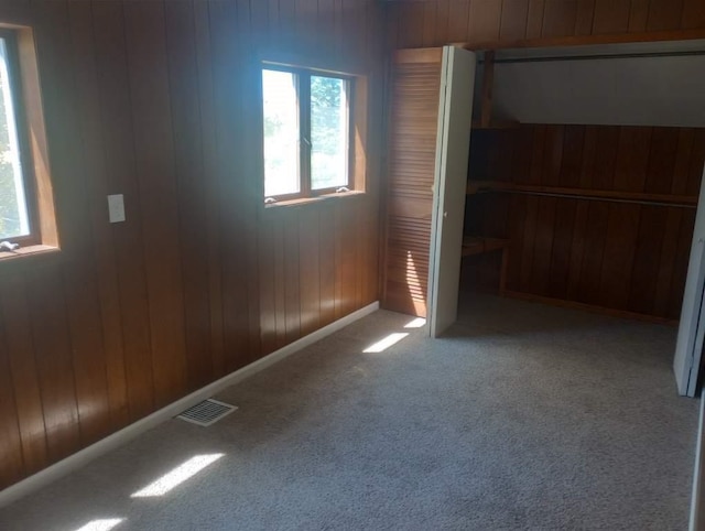 unfurnished bedroom with wood walls, light carpet, and a closet