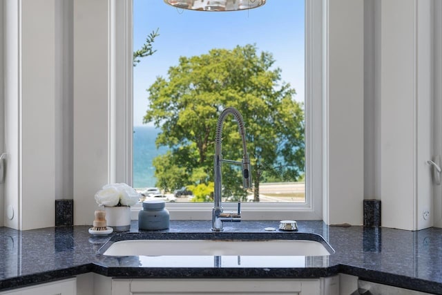 interior details featuring white cabinets, sink, and dark stone counters