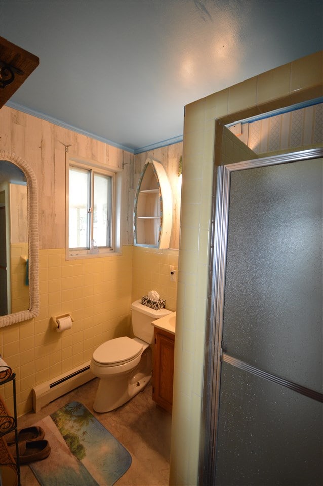 bathroom featuring tile walls, a baseboard heating unit, toilet, and vanity