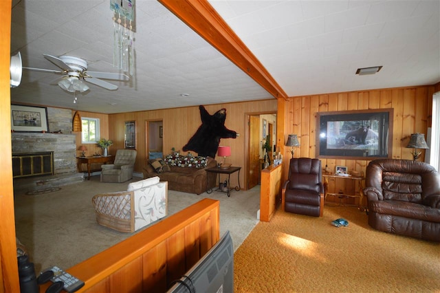 living room with a stone fireplace, light carpet, wood walls, and ceiling fan