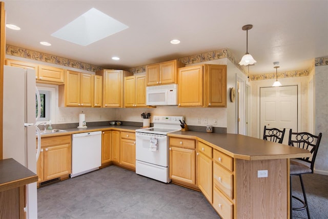 kitchen featuring a skylight, dark tile patterned floors, white appliances, a kitchen breakfast bar, and decorative light fixtures