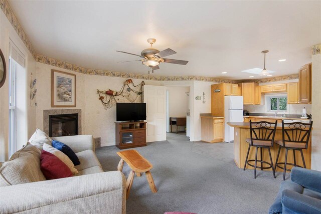 carpeted living room with sink, a tiled fireplace, and ceiling fan