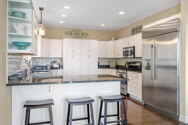 kitchen with a breakfast bar area, appliances with stainless steel finishes, white cabinets, and dark stone countertops