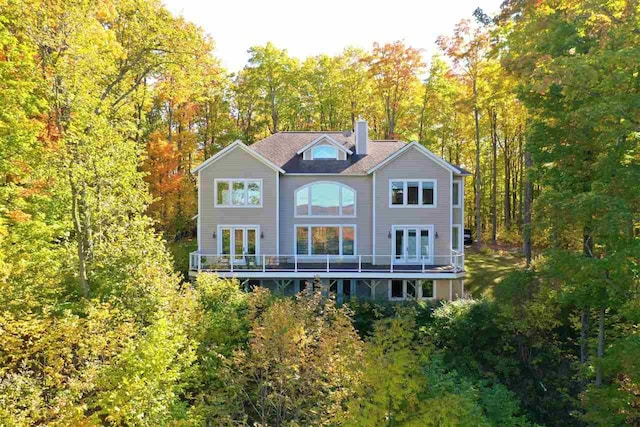 back of property with french doors, a chimney, and a forest view