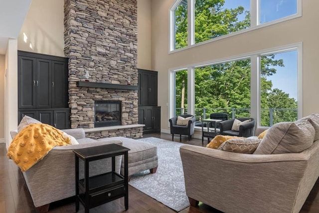 living room with dark wood-style flooring, a fireplace, a towering ceiling, and baseboards