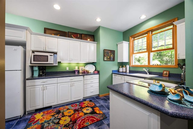 kitchen featuring white appliances, recessed lighting, a sink, white cabinetry, and dark countertops