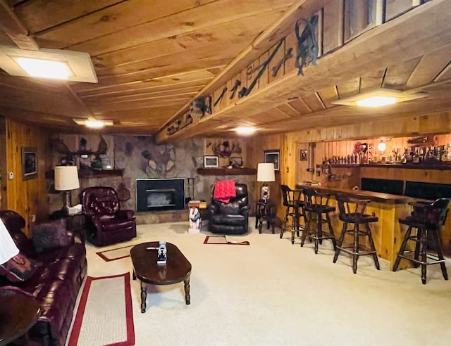 carpeted living room with a fireplace, bar, and wood walls