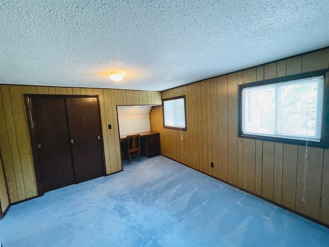 unfurnished bedroom with wood walls, a textured ceiling, and light colored carpet