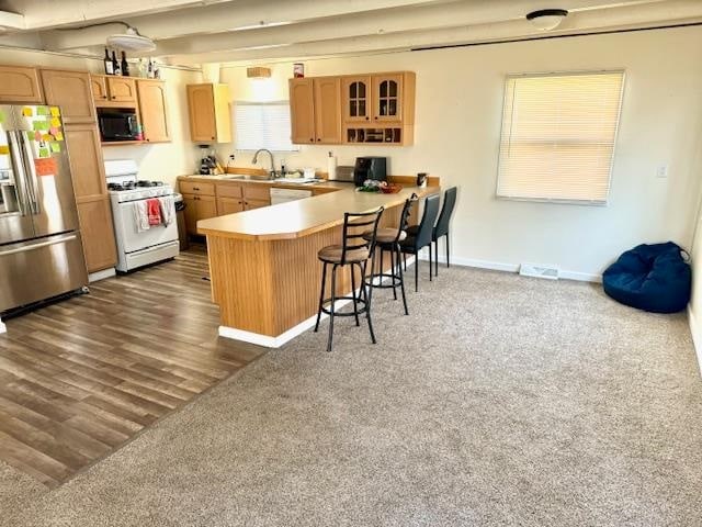 kitchen with white range with gas cooktop, dark hardwood / wood-style floors, stainless steel refrigerator with ice dispenser, a kitchen breakfast bar, and kitchen peninsula