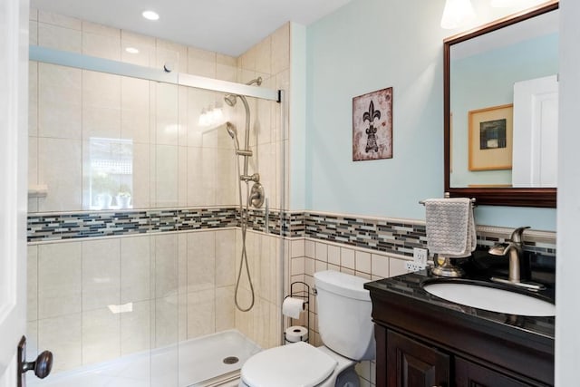 bathroom with tile walls, a shower with shower door, vanity, and toilet