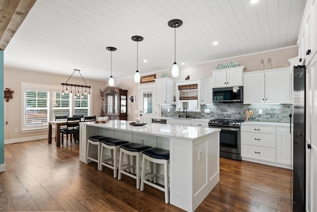 kitchen featuring appliances with stainless steel finishes, decorative light fixtures, a center island, light countertops, and white cabinetry