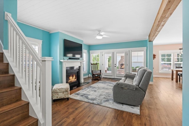 living area featuring crown molding, stairway, a ceiling fan, a glass covered fireplace, and hardwood / wood-style floors