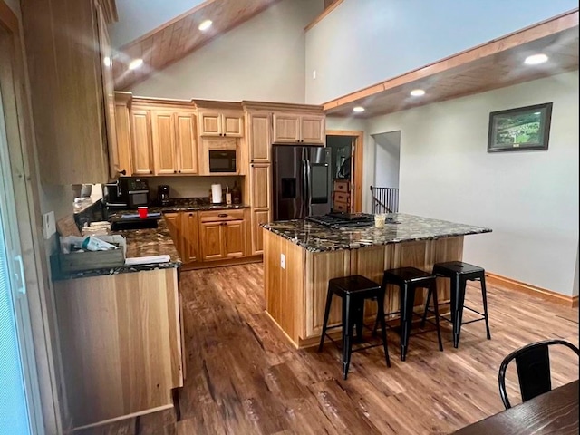 kitchen with dark stone countertops, hardwood / wood-style flooring, a kitchen bar, appliances with stainless steel finishes, and a kitchen island