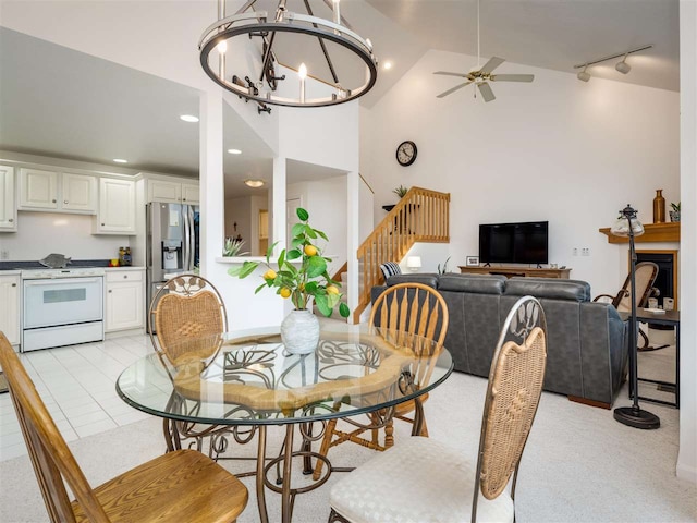 dining space featuring ceiling fan with notable chandelier, light carpet, high vaulted ceiling, and rail lighting