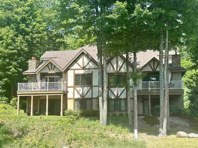 rear view of property featuring a shingled roof, a chimney, and stucco siding