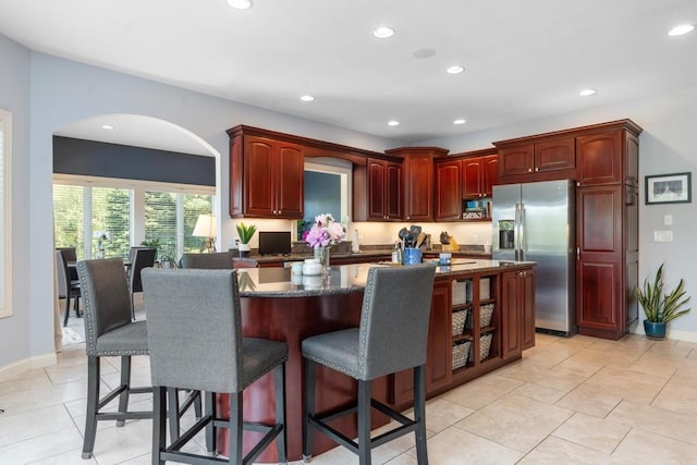 kitchen with a kitchen breakfast bar, stainless steel fridge, a kitchen island, and light tile patterned floors