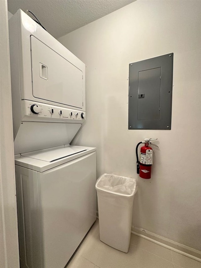 laundry area with electric panel, stacked washer and dryer, and a textured ceiling