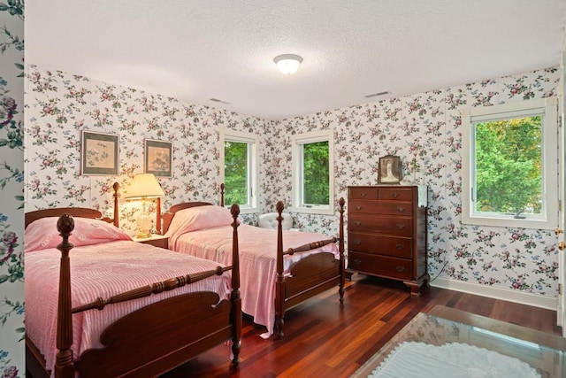 bedroom with dark wood-style floors, baseboards, visible vents, wallpapered walls, and a textured ceiling