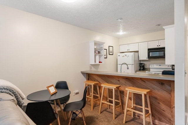 kitchen with dark colored carpet, a breakfast bar area, white cabinetry, kitchen peninsula, and white appliances