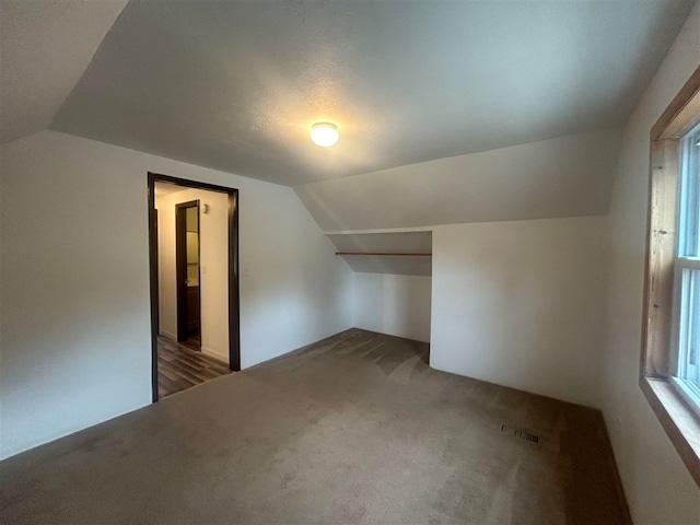 bonus room with a textured ceiling, vaulted ceiling, and dark carpet