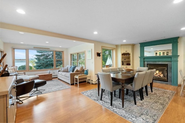 dining room featuring a wealth of natural light, a tiled fireplace, light hardwood / wood-style floors, and baseboard heating