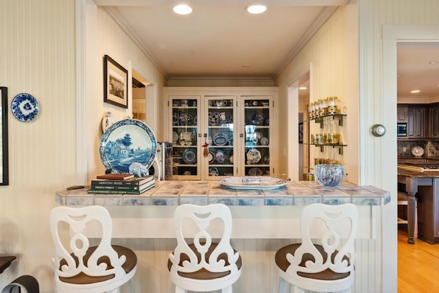 bar featuring crown molding, dark brown cabinetry, decorative backsplash, and light hardwood / wood-style flooring